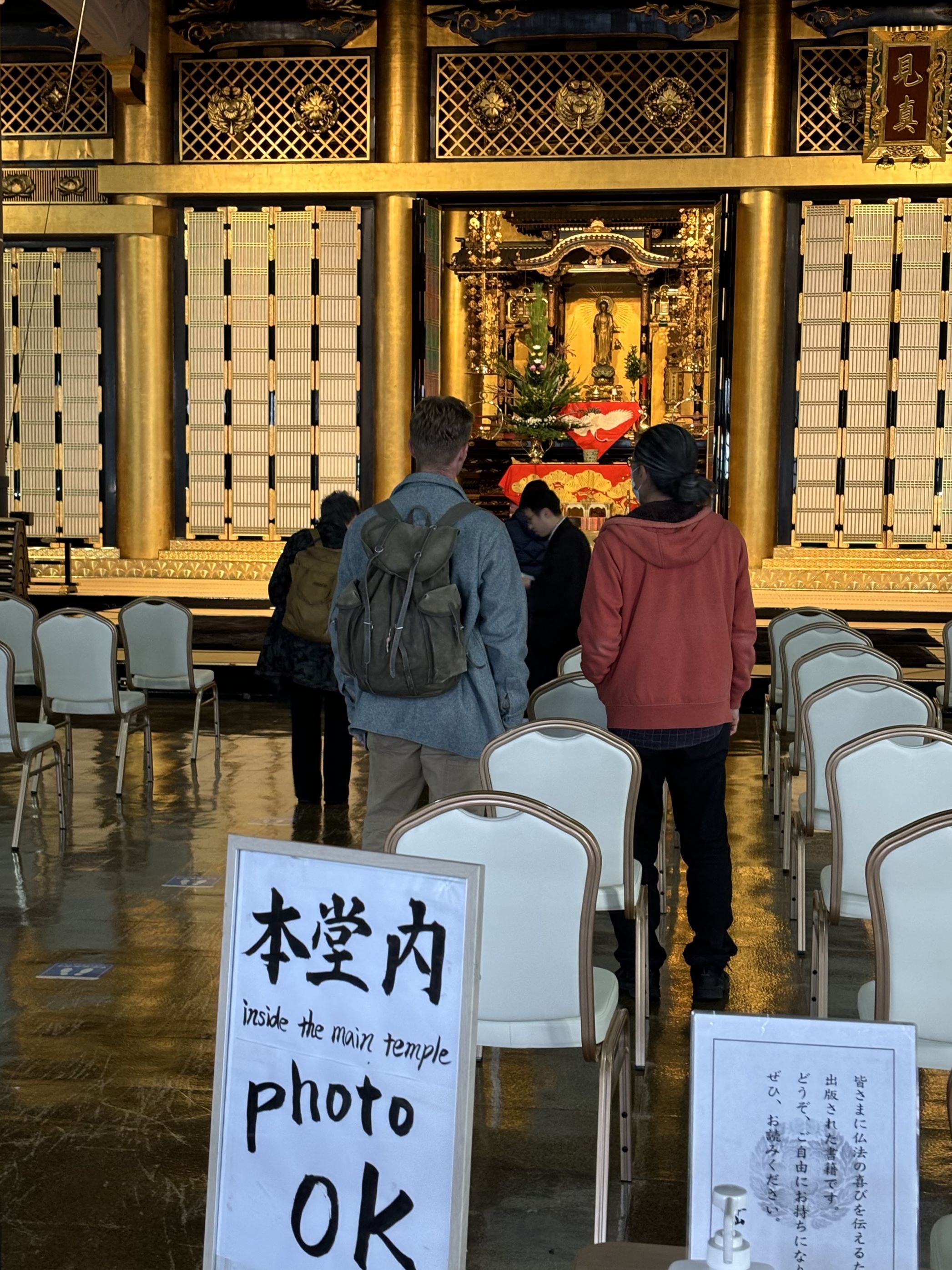 金色的佛堂内景。入口処放置手寫立牌,寫著‘本堂内photo ok’。